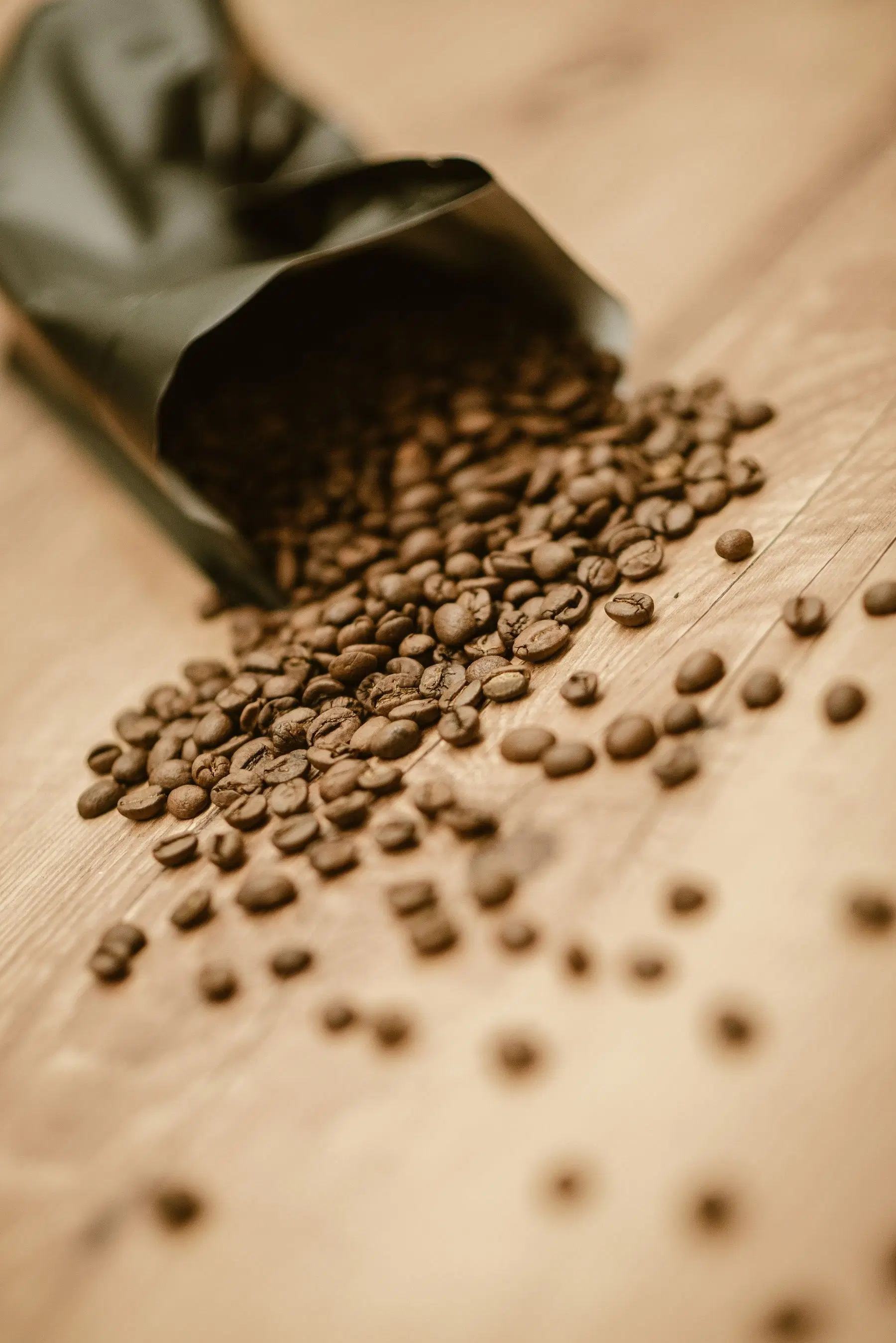 Roasted coffee beans spilling from a bag onto a wooden table